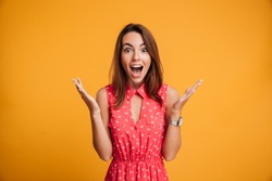 Close-up portrait of young pretty surprised woman with opened mouth standing with open palms, isolated on yellow background