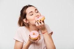 Close up portrait of a satisfied pretty girl eating donuts isolated over white background
