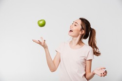 Portrait of a smiling happy girl throwing apple in the air isolated over white background