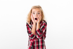 Portrait of a shocked little girl holding hands at her face and looking at camera isolated over white background