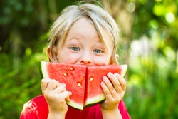 Funny happy child eating watermelon outdoors, making a smile