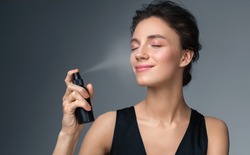 Woman using  finishing spray. Photo of woman with perfect makeup on gray background. Beauty concept