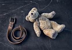 Teddy bear lies on the floor with leather belt, punishment. Parenting through domestic violence. Teddy bear symbolizing a child. The problem of child abuse.