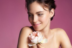 Charming young woman with perfect makeup. Photo of brunette woman with rose on pink background. Skin care concept