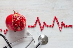 Fruit pomegranate, stethoscope and ECG cardiogram from pomegranate seeds, healthy heart diet concept abstract