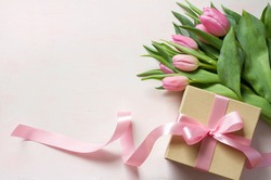 Gift box with long pink ribbon and tulips on light background