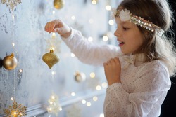 Christmas. Elegantly dressed girl of 8-9 years with delight admires gold Christmas garlands and Christmas-tree decorations. They shine a magic light. Christmas-the mysterious and wonderful time.