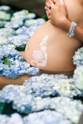 Pregnant woman relaxing in clean outdoor bath with blue hydrangea. Healthy spa treatment with anti-inflammatory and tonic effects. Lifestyle concept.