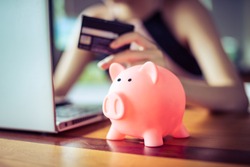 pink color Pig save bank with woman holding credit card using internet computer on background, money discount saving shopping on line concept.