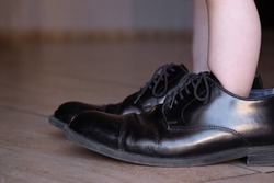 Ambitious Young Child Standing in Dad's Huge Business Shoes with Lots of Room to Spare