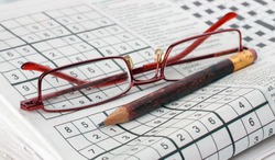 Pencil and glasses on the newspaper with a sudoku game.