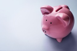 Conceptual financial image with a high angle view of a pink ceramic piggy bank with focus to the coin slot on its back over a grey background with copyspace