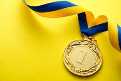 Gold medallion for the winner or champion in a competition or race on a blue and yellow twirled ribbon over a matching yellow background with copyspace