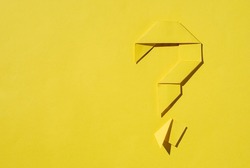 Monochromatic yellow background of a folded paper origami question mark with copy space as a template for conceptual themes