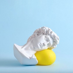 The head and face of David of an antique statue lies on a yellow balloon as a minimal trend concept of vaporwave surreal or sleep.