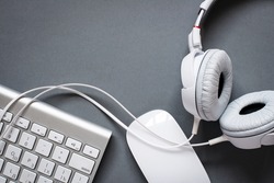 High Angle View of Modern White Audio Headphones with Cord, Mac Computer Keyboard and Mouse on Grey Desk Background with Copy Space