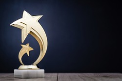 Elegant gold winners trophy with shooting stars to be awarded for the first place in a competition or championship over a dark blue background with copy space
