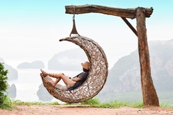 Relaxed woman girl sit on the moon shape wooden swing with island and mountain lanscape view in Pang Nga, Samed Nangshe, Thailand