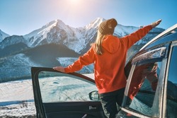 Woman traveling exploring, enjoying the view of the mountains, landscape, lifestyle concept winter vacation outdoors. Female standing near the car in sunny day, travel in the mountains, freedom