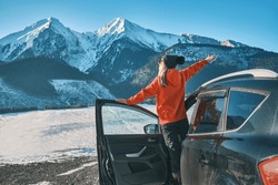 Woman traveling exploring, enjoying the view of the mountains, landscape, lifestyle concept winter vacation outdoors. Female standing near the car in sunny day, travel in the mountains, freedom.