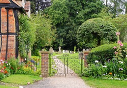 Wrought Iron Gate to an English Churchyard and Cemetery with cottage and flower filled garden