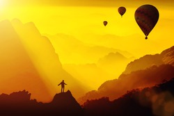 Silhouette of young traveler standing on top of mountain with amazing Fantasy sunset with hot air balloons.Travel Lifestyle success concept,adventure active vacation outdoor,happiness freedom emotion.