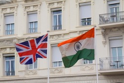 UK Great Britain and India national flag waving in the wind from flagpoles in front of a white mansion.