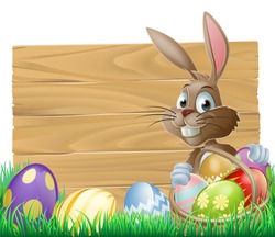 The Easter bunny with a basket of Easter eggs with more Easter eggs around him by a wood sign board