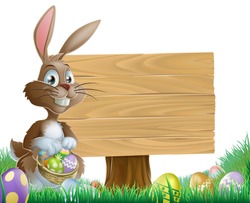 The Easter bunny holding a basket of Easter eggs with more Easter eggs around him by a wood sign board