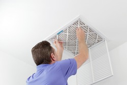 Person Removing Ceiling Air Filter. Caucasian male removing a square pleated dirty air filter with both hands from a ceiling duct. Guy taking out an unclean air filter from a home ceiling air vent