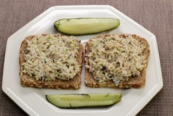 Two open-faced chicken salad sandwiches on a plate with dill pickle spears close-up. Chicken salad open-faced sandwiches on sprouted grain bread with dill pickle spears on an octagon plate close-up.