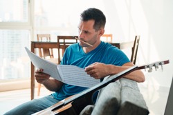 Mid Adult Man Reading Acoustic Guitar Sheet Music In Apartment