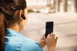 Mid adult hispanic person with mobile phone and bluetooth headset, typing on telephone in the street