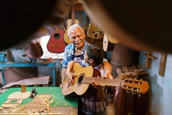 Small family business and traditions: old grandpa with grandson in lute maker shop. The senior artisan gives teaches how to play classic guitar to the boy, who plays his first musical notes 