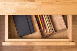 Notebook and pencils in open desk drawer top view image. Drawing background