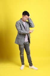 The Asian LGBTQ man with grey blazer standing on the yellow background.