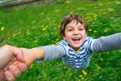 Portrait of a happy, laughing boy being held and spun around in the garden with yellow flowers background