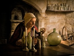 Woman in medieval outfit working as an alchemist or witch in the kitchen of a French medieval castle - with property release