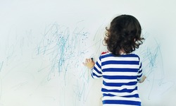 Curly cute little baby girl drawing with crayon color on the wall. Works of child