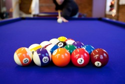Man gets ready to begin breaking the rack of balls in a billiard game of 8 ball. Very shallow depth of field with sharpest focus on the eight ball.
