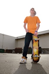 A young teenage skateboarding standing with his skateboard in an urban setting.