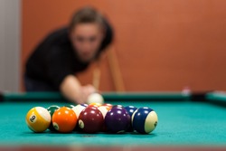 A young man lines up his shot as he breaks the balls for the start of a game of billiards. Shallow depth of field.