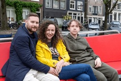 A man, woman and their son sit on a bench in a boat that sails on a canal in the city of Amsterdam