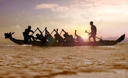 Silhouette of a Dragon boat with people paddling at sunset 