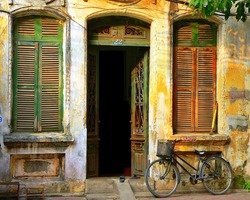 An Old, Decaying House with open door and shutters on the windows and a bicycle in Hanoi, Vietnam. Image by Kevin Hellon.