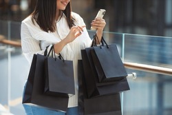 No face portrait of beautiful plus size woman happy with many purchases in paper bags bought on sale in a shopping mall and writing message in smartphone