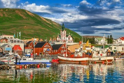 Beautiful view of the historic town of Husavik with traditional colorful houses and traditional fisherman boats lying in the harbor in golden evening light at sunset, northern coast of Iceland