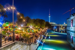 People dancing at summer Strandbar beach party near Spree river at historic Museum Island with famous TV tower in the background in twilight during blue hour at dusk, Berlin Mitte district, Germany