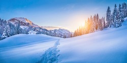 Panoramic view of beautiful winter wonderland mountain scenery with traditional mountain cabin the background in the Alps in golden evening light at sunset