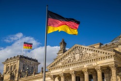 German flags waving in the wind at famous Reichstag building, seat of the German Parliament (Deutscher Bundestag), on a sunny day with blue sky and clouds, central Berlin Mitte district, Germany